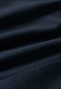 Marineblauwe stof met een gladde textuur, voorzien van subtiele horizontale plooien en een zichtbare naad; het materiaal lijkt zacht en lichtgewicht te zijn.
