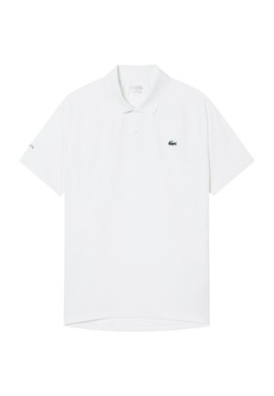 Polo blanc à manches courtes avec col, patte de boutonnage à deux boutons, petit logo crocodile vert sur le côté gauche de la poitrine et texte Lacoste sur la manche gauche.