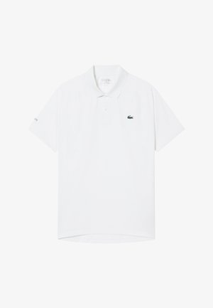 Polo blanc à manches courtes avec col, patte de boutonnage à deux boutons, petit logo crocodile vert sur le côté gauche de la poitrine et texte Lacoste sur la manche gauche.