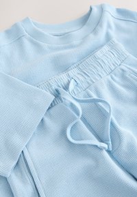 Sudadera de tela acanalada azul claro y pantalones a juego con cordón, extendidos planos mostrando textura y detalles de la cintura.