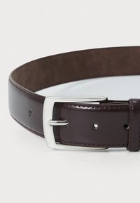 Cinturón de cuero marrón con textura suave, que presenta una hebilla de metal plateado y detalles de costura. Múltiples agujeros para ajustar el tamaño.