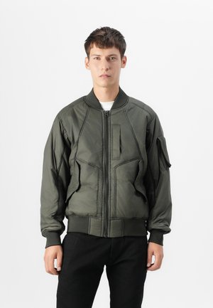 Casaco bomber verde-azeitona com fecho éclair frontal, punhos canelados e um bolso utilitário. Apresenta uma superfície texturizada e detalhes de costura.