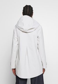 Bílá bunda s kapucí a řaseným zadním dílem, s dlouhými rukávy a manžetami na knoflíky. Hladká, lehká tkanina s čistým designem.