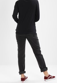 Camisa de manga larga negra, vaqueros grises con puños enrollados y zapatillas rojas. Tejido suave con un corte relajado. Enfoque en las piernas desde la vista trasera.
