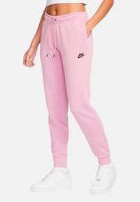 Rosa sweatsbyxor med ett elastiskt midjeband, snörning, sidofickor och en liten svart Nike-logga på vänstra låret. Matchas med vita sneakers.