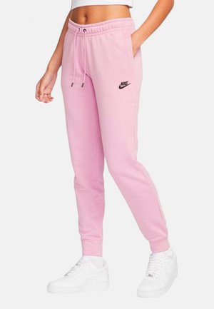 Roze trainingsbroek met een elastische tailleband, een trekkoord, zijzakken en een klein zwart Nike-logo op de linker bovenbeen. Gekoppeld met witte sneakers.