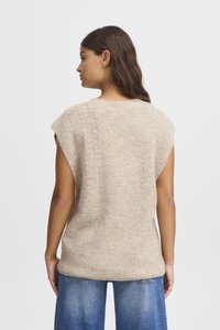  krómbordó kötött pulóver, amely rövid ujjú, hátul texturált mintázattal és bordázott szegéllyel rendelkezik. Kék denim farmernadrággal párosítva.