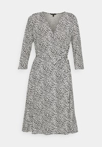 Schwarz-weiß gepunktetes Kleid mit V-Ausschnitt, langen Ärmeln und Bindegürtel, aus leichtem Stoff hergestellt. Ausgestellter Saum unterhalb des Knies.