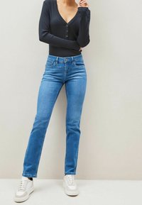Blue denim jeans with a straight-leg cut, belt loops, five pockets, and a button closure, paired with white sneakers.