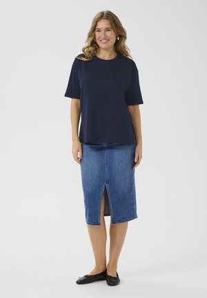 Marineblaues T-Shirt mit kurzen Ärmeln, kombiniert mit einem knielangen Jeansrock mit Schlitzen vorne, getragen mit schwarzen, flachen Schuhen.