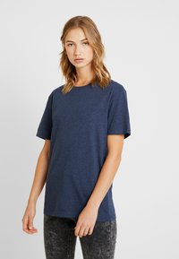 T-shirt a maniche corte blu navy realizzato in tessuto morbido, con scollatura rotonda e vestibilità comoda. Abbinato a jeans scuri e sbiaditi.
