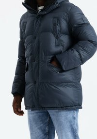 Giacca imbottita blu navy scuro con cappuccio, dotata di zip frontale, bottoni a pressione e due tasche davanti. Realizzata in materiale lucido trapuntato.