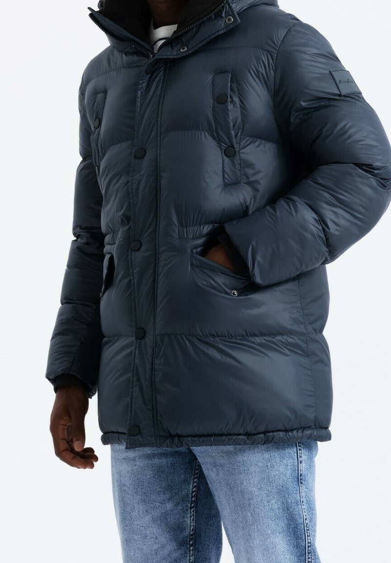 Giacca imbottita blu navy scuro con cappuccio, dotata di zip frontale, bottoni a pressione e due tasche davanti. Realizzata in materiale lucido trapuntato.