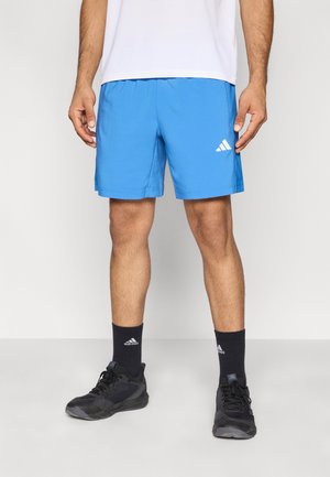 Sinised sportlikud lühikesed püksid, valmistatud kergest kangast, millel on elastne vöökoht ja valge logo vasakul säärel. Kandmisega mustad jalanõud ja sokid.