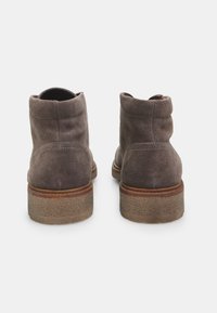 Botas de tobillo de ante gris con punta redondeada, paneles laterales elásticos y una suela marrón texturizada. Presenta detalles de costura sutiles en la parte superior.