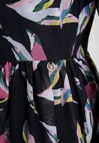 Gros plan d'une robe en tissu noir avec un imprimé floral abstrait rose, vert, bleu et jaune et un petit bouton métallique rond à la taille.