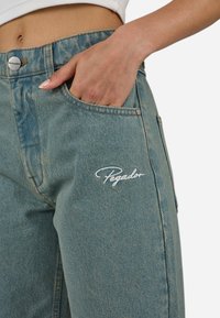 Ljust blå denimjeans med avslappnad passform, synlig sömnad och bakfickor. "Pegador" broderat i vitt på låret.