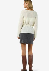 Maglione lavorato a maglia color crema con vestibilità comoda e vita con cintura, abbinato a una gonna di jeans grigia e stivali di pelle marrone alti fino al ginocchio.