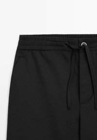 Pantaloni jogger neri con cintura elastica, cordoncino regolabile e tasche laterali. Realizzati in un tessuto morbido e testurizzato.
