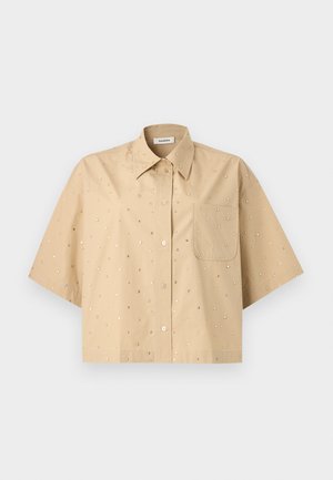 Beige overhemd met korte mouwen en knopen, puntige kraag, borstzak en kleine reflecterende stippen verspreid over de stof.