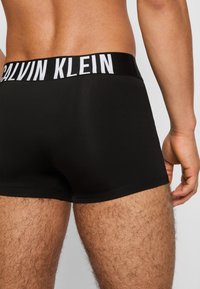 Schwarze Baumwoll-Boxershorts mit einem Calvin Klein-Logo am Bund. Glatte Textur, enganliegendes Design, kurze Beinlänge und minimalistischer Stil.
