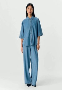 Chemise en denim et pantalons large en bleu clair. Design à boutons avec un col et des manches courtes. Texture lisse avec des accents minimalistes.