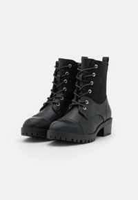 Botines negros de cuero y ante, con puntera redonda, cordones, ojales plateados y un tacón bajo.