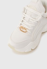Hvide sneakers med glat læderoverdel, tyk sål og dekorativ guldkædeaccent på snørebåndene. Har branding på tungen.