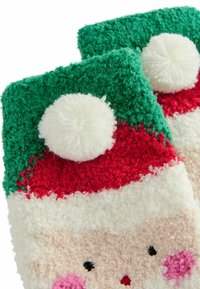 Fuzzy julluvor i röd, grön och vit. Har en vit pom-pom och ett ansikte med rosa kinder, mot en texturerad bakgrund.