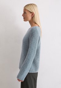 Jasnoniebieski sweter o miękkiej, puszystej fakturze, szerokim dekolcie i długich rękawach. Stylizowany z ciemnymi, prążkowanymi spodniami.