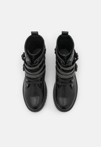 Botas negras de piel hasta el tobillo con correas texturizadas y tachuelas, punta redonda y tirador trasero. Superficie lisa con detalles de herrajes en contraste.
