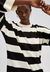 Jersey de rayas en blanco y negro con un escote redondo de canalé y mangas oversize, que presenta una textura de punto suave y patrones contrastantes en negrita.