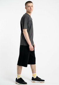 Ciemnoszary t-shirt z krótkim rękawem, czarne szorty do kolan, czarne sneakersy z gumową podeszwą i skarpetki w żółte paski.