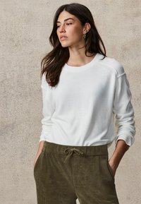 Witte gebreide trui met een ronde hals en ribgebreide manchetten, gecombineerd met olijfgroene corduroybroek met een koord in de taille.