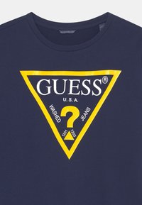 Granatowa bawełniana koszulka z dużym żółtym trójkątnym logo z napisem "GUESS U.S.A." oraz czarnym detalem "WASHED JEANS" wewnątrz.