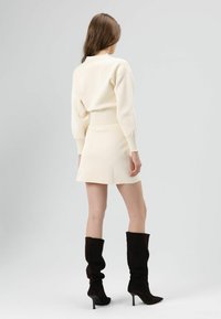 Crèmekleurige set van een geribbelde gebreide trui en minirok. Trui met lange mouwen en een colletje. Paar zwart suède kniehoge laarzen met hak.