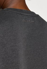 Tumehallist puuvillast T-särk, millel on soonikkoes krae, sisaldades peent "ONLY PLAY" tikandit kaela tagaosa lähedal ning sujuvat tekstuuri.