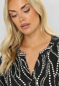 Svart skjorta med vitt abstrakt mönster, knapp-up halslinning och mjuk tygtextur. Har en klassisk krage och mjuk fall.