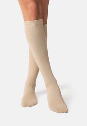 Knæstrømper lavet af et blødt, ribbet stof i en neutral beige farve, med en glat tekstur og et tætsiddende design, der går op over læggen.