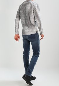 Camicia a maniche lunghe grigia e bianca a righe, abbinata a jeans skinny blu e stivaletti neri alla caviglia, vista da dietro, che mette in evidenza un look casual.
