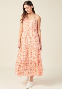 Maxi mekko, jossa on oranssia ja valkoisia kuvioita, ohuilla olkaimilla, rypytetty yläosa ja täysimittainen hame; yhdistettynä valkoisiin lenkkareihin.