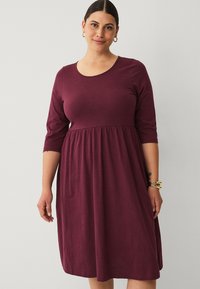 Bordeaux jurk tot de knie met een ronde halslijn en driekwartmouwen, met een geplooide taille voor een ontspannen pasvorm en een zachte textuur.