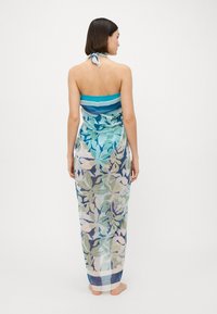 Sarong multicolor con un estampado botánico que presenta tonos de azul, verde y beige. Tela transparente, diseño tipo halter y parte superior con banda.