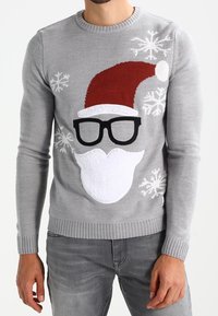 Mann trägt einen grauen Weihnachtspullover mit Weihnachtsmannmütze, Bart, schwarzen Brillen und weißen Schneeflockenmustern.