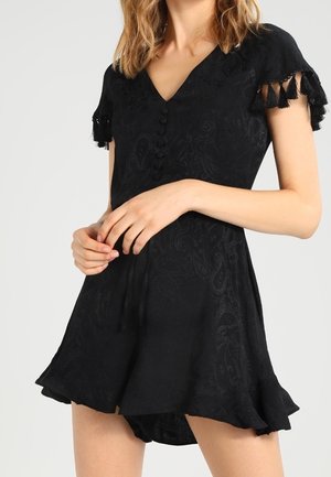 Musta mekko lyhyillä hihoilla, jossa on V-pääntie, napitusyksityiskohta ja fringein. Valmistettu teksturoidusta kankaasta, jossa on paisley-kuvio.