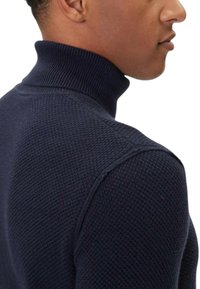Maglione dolcevita in maglia blu navy con superficie testurizzata, collo a coste e design aderente, che enfatizza calore e comfort.