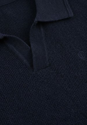 Cuello de polo de punto en azul marino oscuro con textura de gofre y un sutil logo bordado en el pecho.