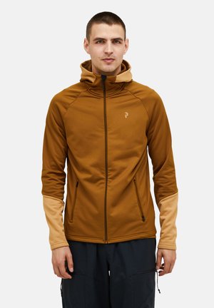 Bruine ritsjack met hoge kraag, contrasterende beige mouwen, zijritszakken en een klein logo op de borst. Gladde textuur.