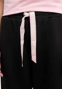 Schwarze Sweatpants mit einer weichen Textur, ausgestattet mit einem rosa Markenband zum Binden an der Taille, das mit "BRUNO BANANI" beschriftet ist. Verstellbarer elastischer Bund.