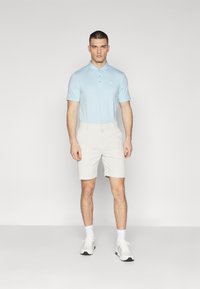 Lys blå polo-skjorte med korte ermer og krage, kombinert med beige shorts. Brukes med hvite treningssko og sokker. Enkel og uformell design.